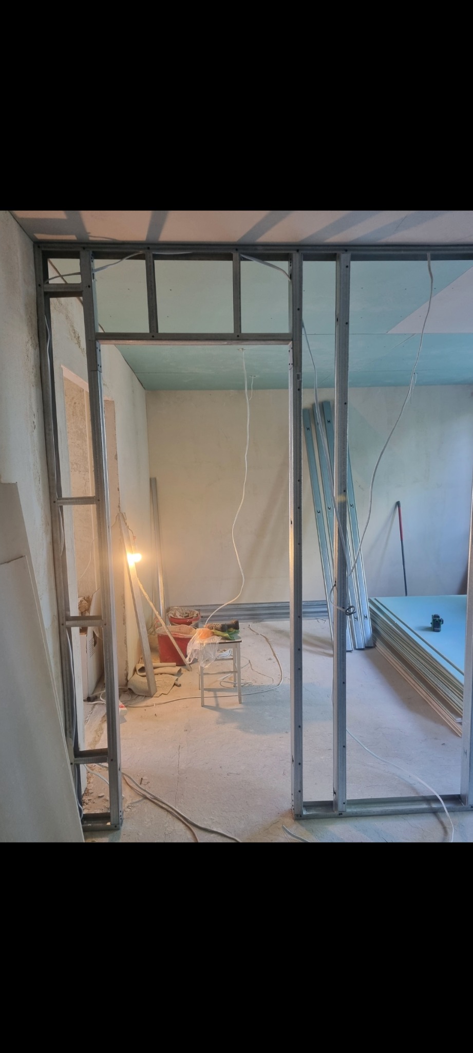 Stelaż z profili metalowych pod ściankę działową z płyt gipsowo-kartonowych w trakcie montażu, widoczne płyty G-K i narzędzia na zapleczu.