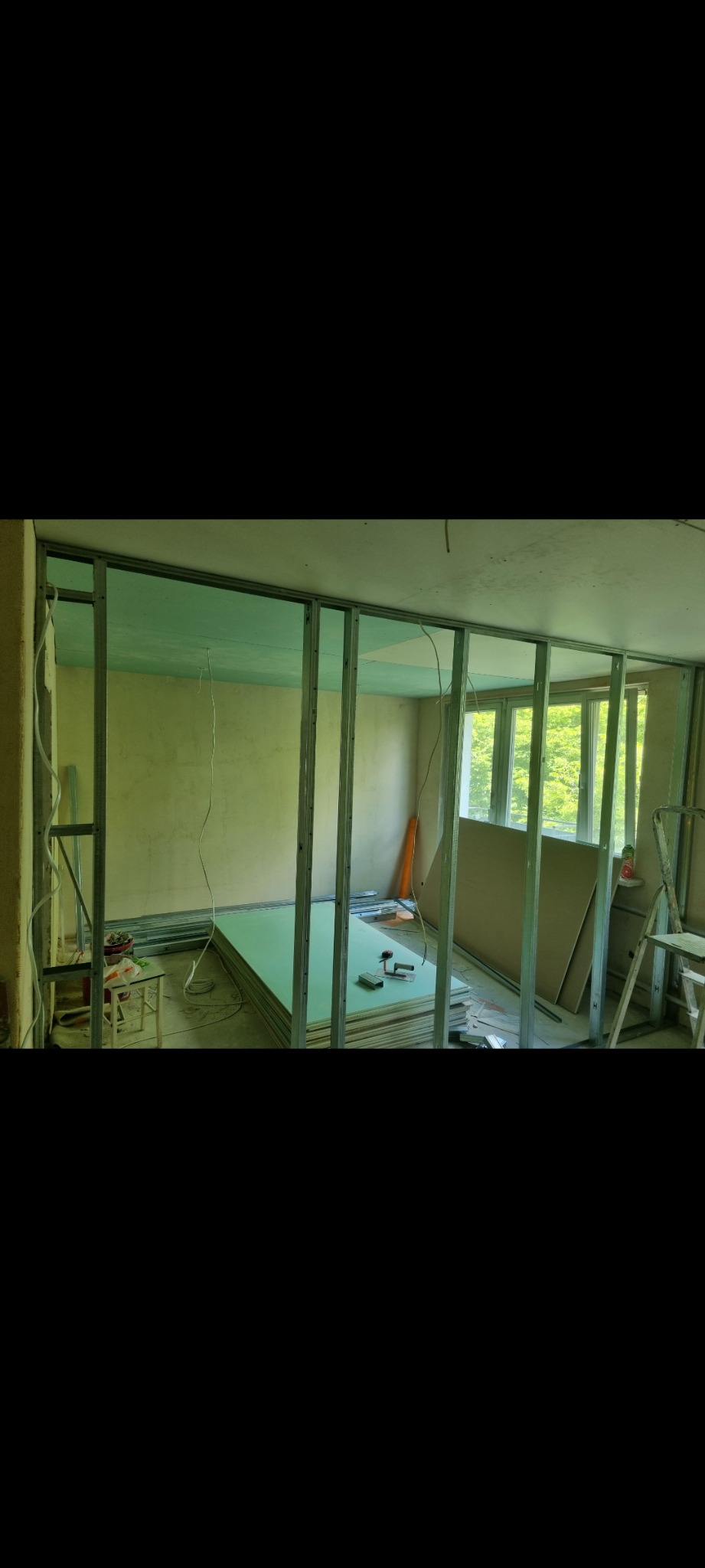 Montaż metalowego stelażu pod płytę karton gips na suficie i ścianach, widoczne płyty gipsowe, narzędzia i drabina.