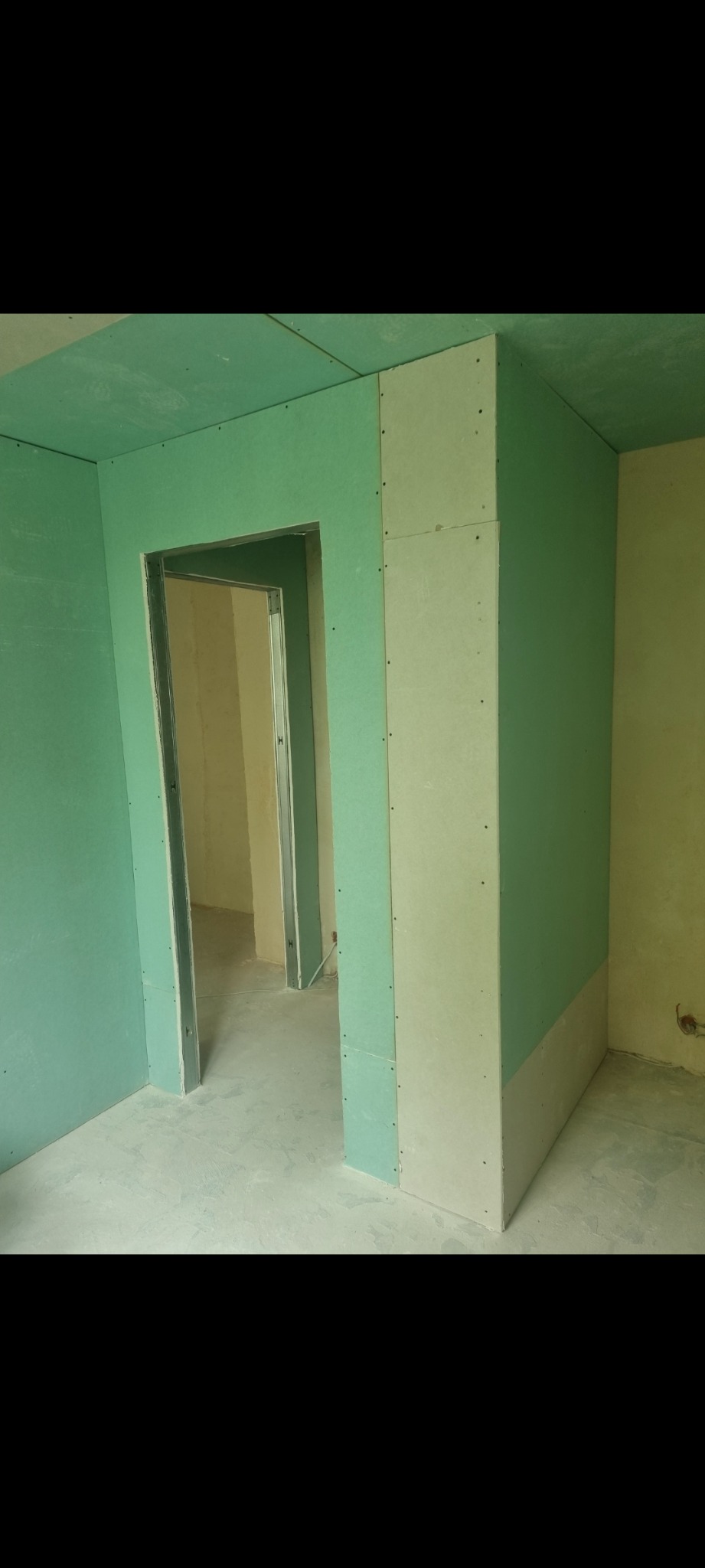 Wnętrze w trakcie montażu ścian działowych i sufitu z zielonych płyt gipsowo-kartonowych, widoczne metalowe profile ościeżnic drzwiowych.