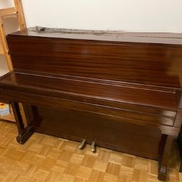 Brum brum Przeprowadzki - Antyczne, mahoniowe pianino z pawim piórem na górze, stojące na parkiecie w pokoju z regałami w tle.