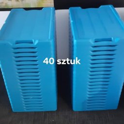 Brum brum Przeprowadzki - Dwa niebieskie pojemniki plastikowe z otworami wentylacyjnymi, ułożone obok siebie z napisem '40 sztuk', na tle ściany z obrazem górskiego krajobrazu i czarnego panelu.