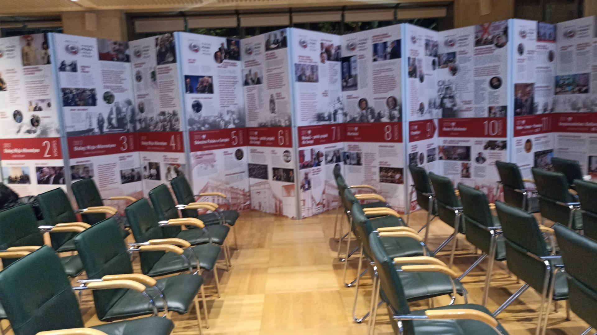 Sala konferencyjna z rzędami krzeseł i ściankami informacyjnymi prezentującymi historię, przygotowana do wydarzenia.