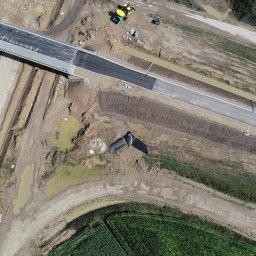 Geo-Control Tobiasz Gałazka - Zdjęcie z drona: budowa drogi z mostem, widoczne maszyny, teren budowy i fragmenty zieleni. Ujęcie z góry, ukazujące postęp prac.