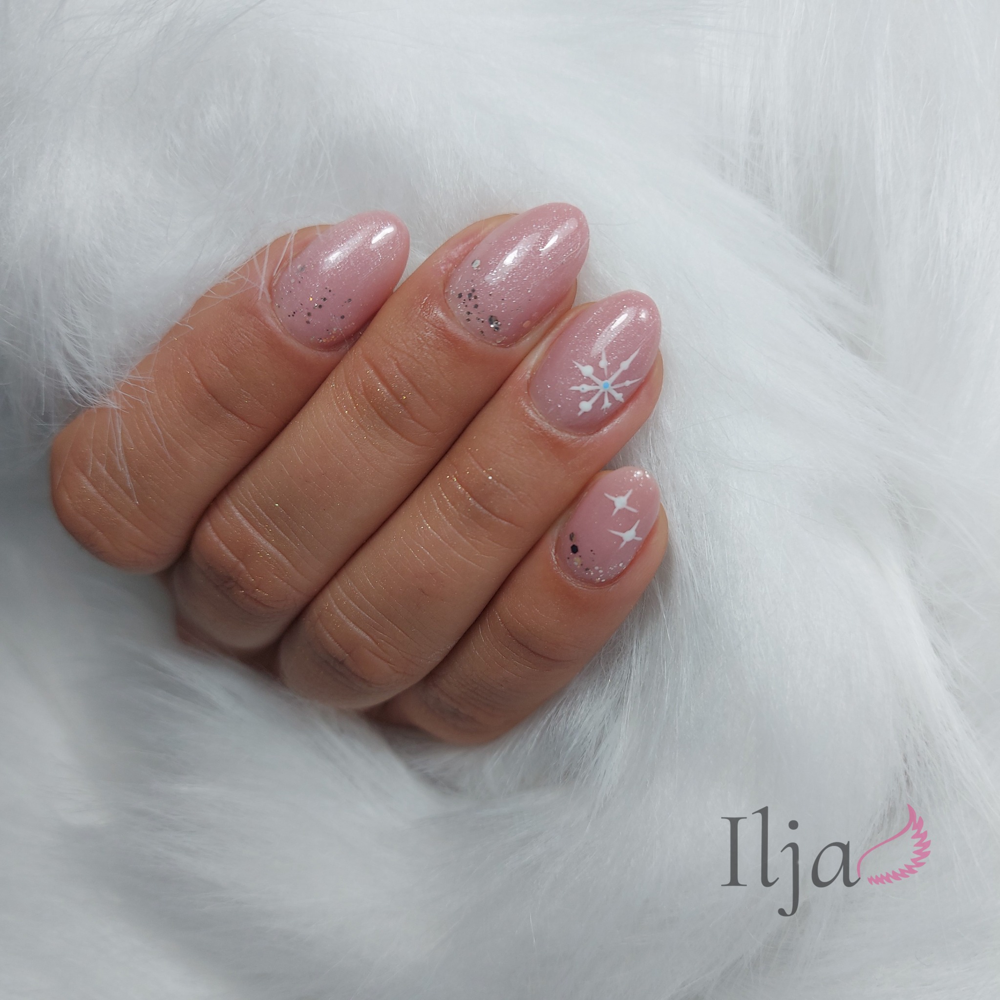 Dłoń z owalnymi paznokciami w kolorze pudrowego różu, zdobionymi srebrnym brokatem i motywem białej śnieżynki na tle białego, puszystego futerka.