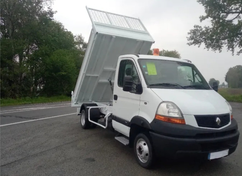 Biała wywrotka Renault Master z podniesioną skrzynią ładunkową, zaparkowana na poboczu drogi w pochmurny dzień.