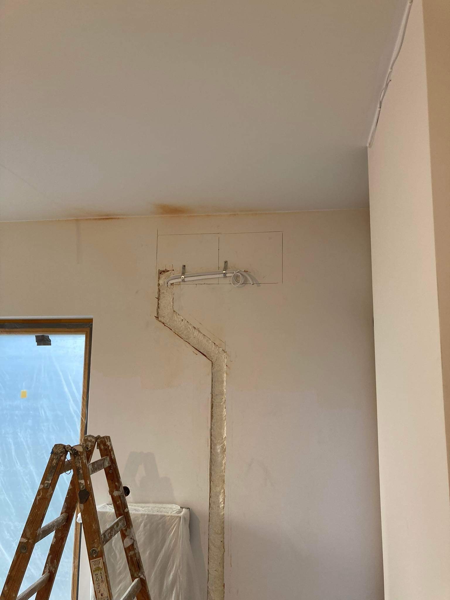Przygotowanie pod instalację przewodów w ścianie, widoczne wycięte bruzdy, przewody przymocowane do ściany oraz drabina malarska w pomieszczeniu w trakcie remontu.