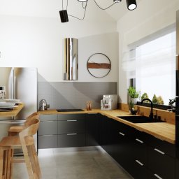 Jasny Kąt/Nemesis - Nowoczesna kuchnia z czarnymi szafkami, drewnianym blatem i akcentami w kolorze drewna, oświetlona lampami sufitowymi i światłem dziennym z dużego okna.