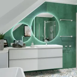Nowoczesna łazienka na poddaszu z zielonymi ścianami, okrągłym lustrem z podświetleniem LED, białą szafką pod umywalką i kolorową mozaiką na podłodze. Widoczna kabina prysznicowa i logo firmy...