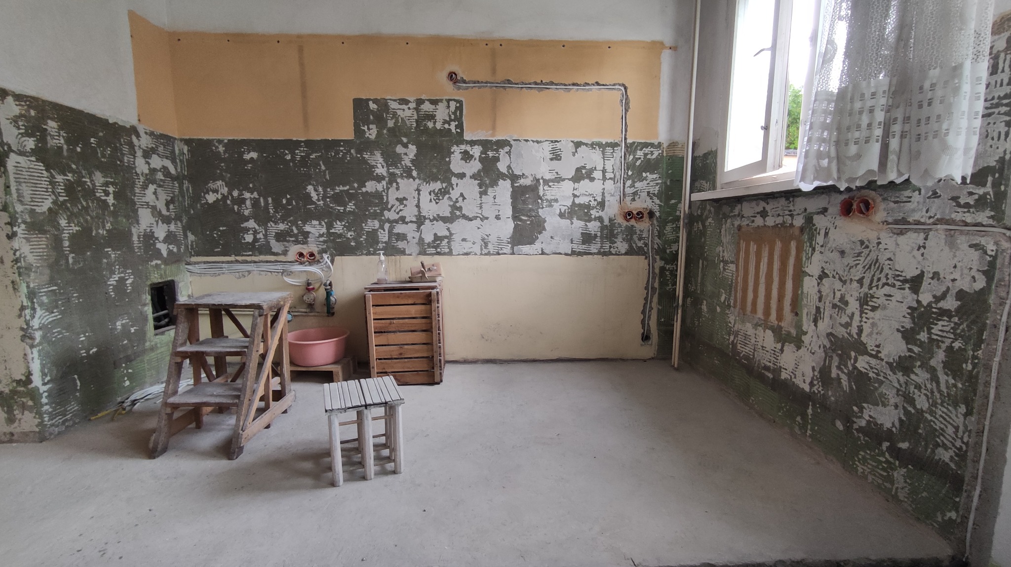 Pokój w trakcie remontu z odsłoniętymi przewodami elektrycznymi w ścianie, widoczne puszki instalacyjne, drabina malarska i stolik.