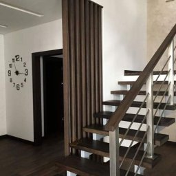 Lisa coffee Oleksander Yermolenko - Nowoczesne schody z ciemnego drewna z metalową balustradą, widok na ścianę z zegarem i dekoracyjną drewnianą ścianką działową.