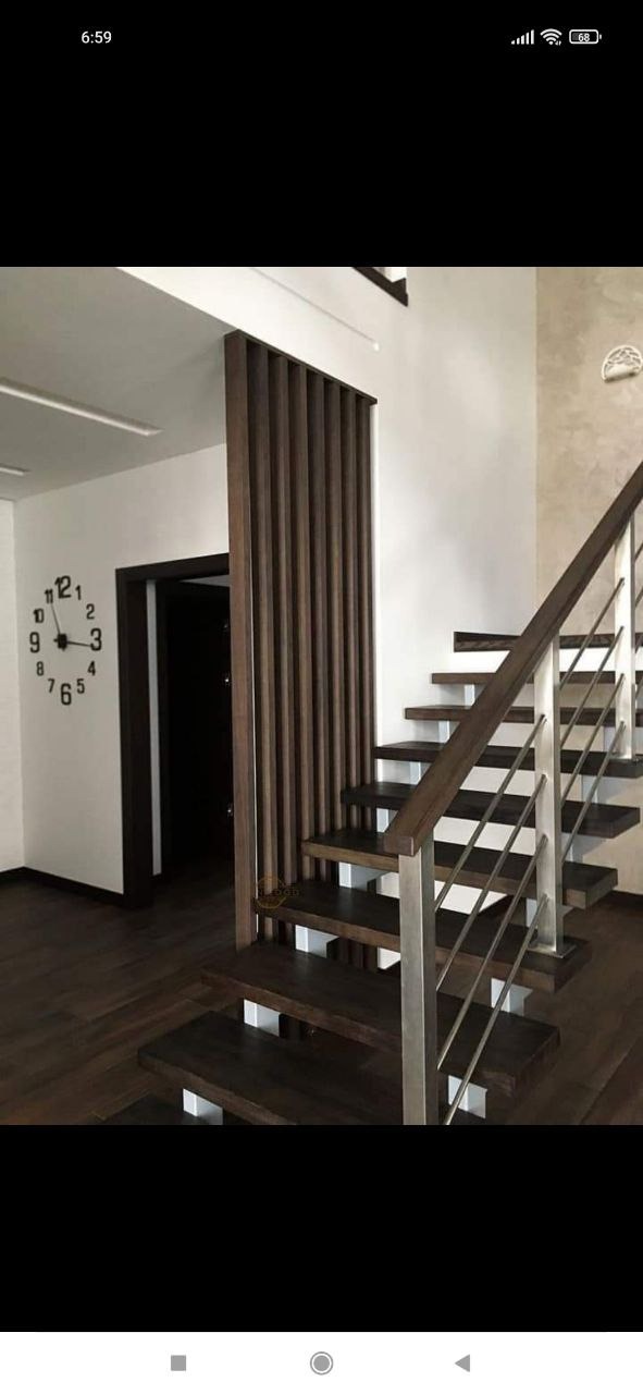 Nowoczesne schody z ciemnego drewna z metalową balustradą, widok na ścianę z zegarem i dekoracyjną drewnianą ścianką działową.