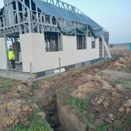 KLN Mirosław Markowiak - Konstrukcja domu ze stalowym szkieletem w trakcie budowy, widoczny pracownik w odblaskowej kurtce, częściowo ocieplone ściany, wykopany rów w ziemi.