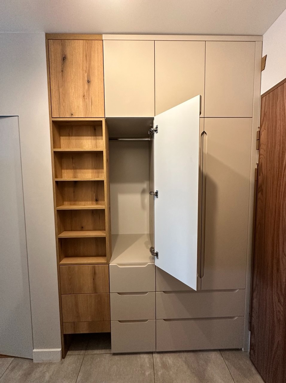 Warszawa: Szafa na wymiar z otwartą półką i szufladami w odcieniach beżu i drewna. Jedno skrzydło drzwi szafy jest otwarte, ukazując wnętrze.