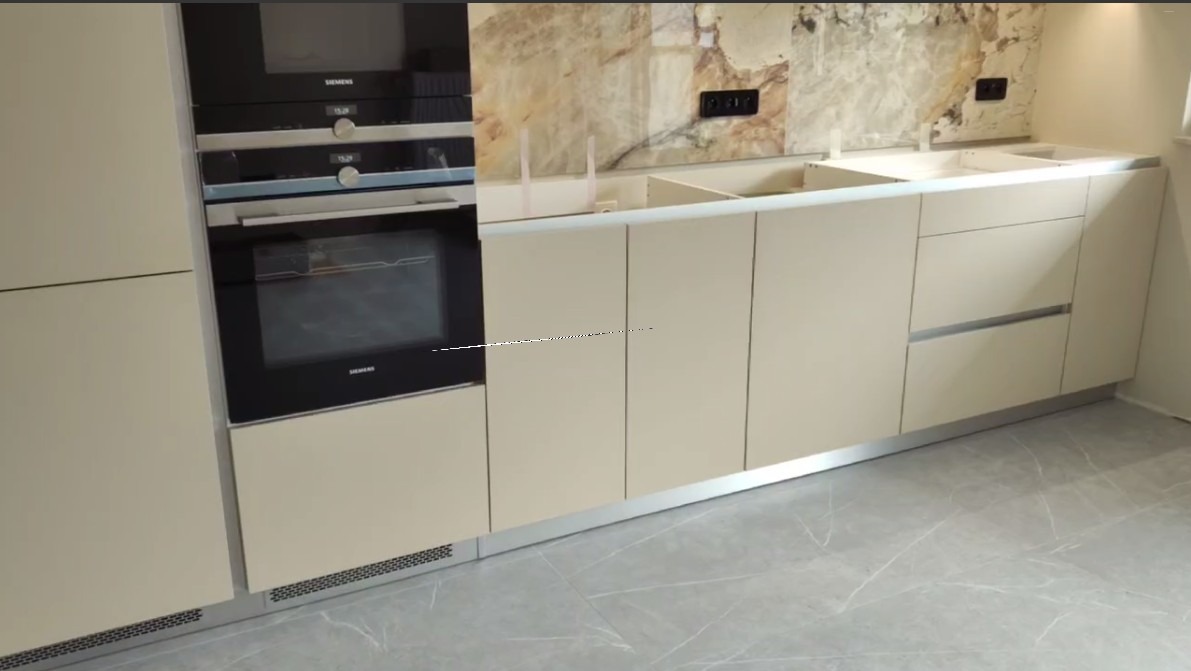 Kremowa zabudowa kuchenna z piekarnikiem Siemens i marmurowym blatem, widok z dołu, nowoczesny styl, szare płytki podłogowe.