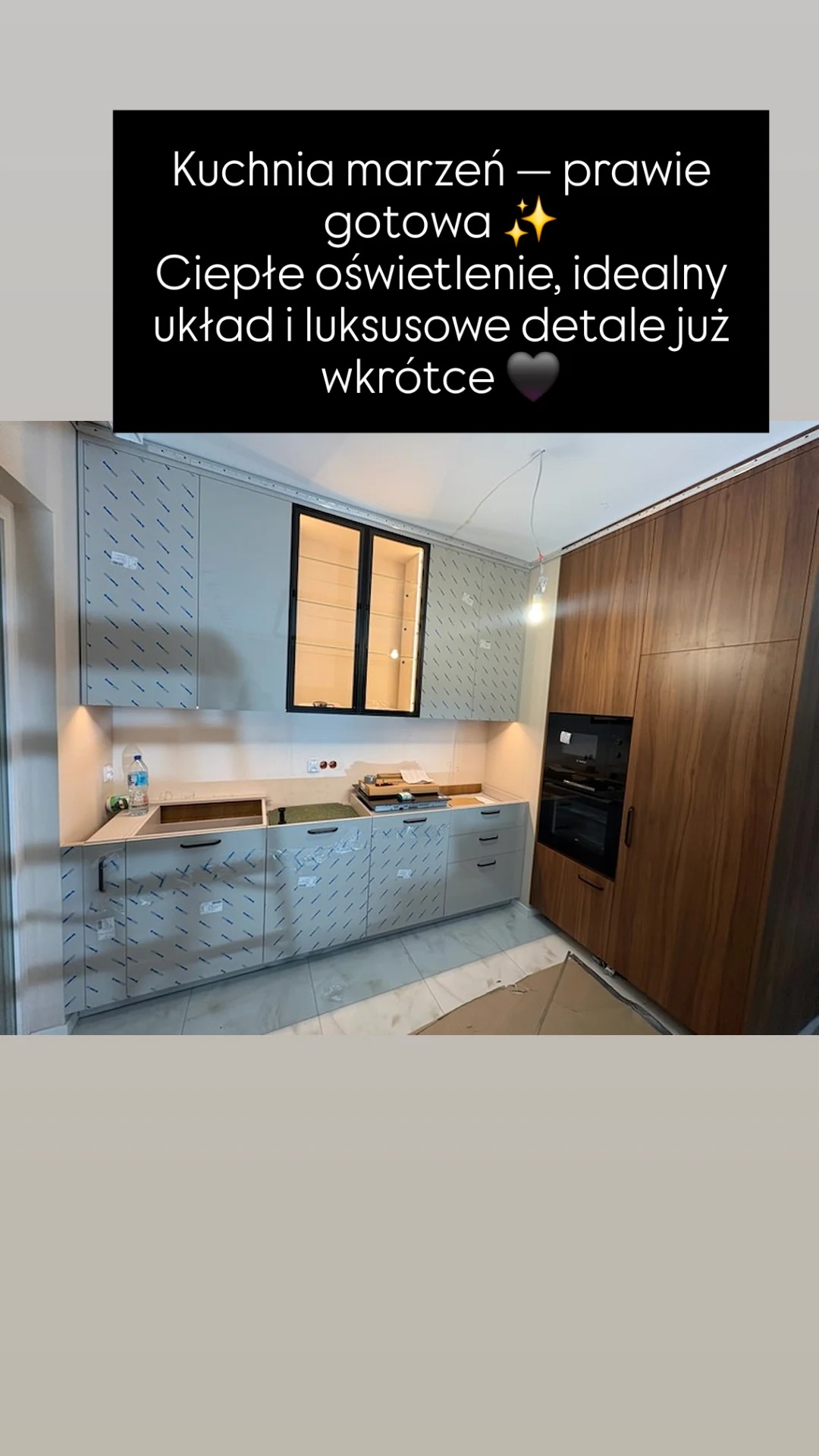 Montaż kuchni: szare szafki z folią ochronną, drewniana zabudowa z piekarnikiem, ciepłe oświetlenie. Etap końcowy, luksusowe detale wkrótce.