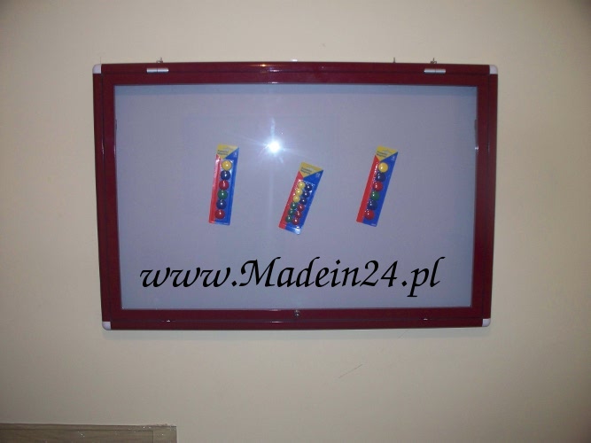 Bordowa tablica ogłoszeniowa z trzema opakowaniami kolorowych magnesów i adresem strony internetowej.