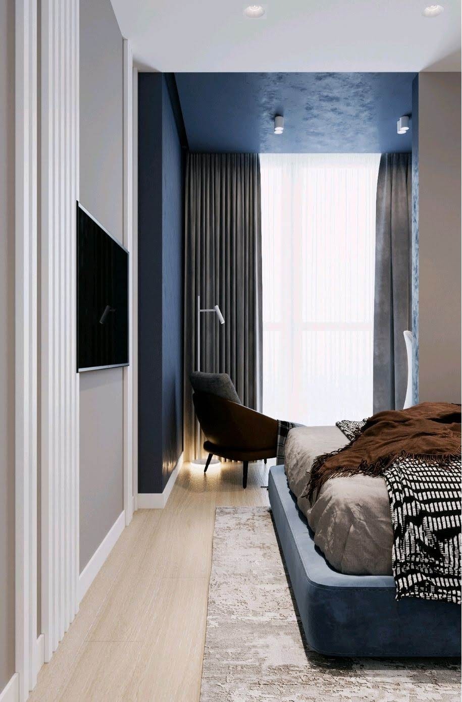Nowoczesna sypialnia w Krakowie z akcentami granatu i szarości: łóżko na platformie, fotel z brązowej skóry, minimalistyczna lampa podłogowa i telewizor na ścianie z dekoracyjnymi listwami.