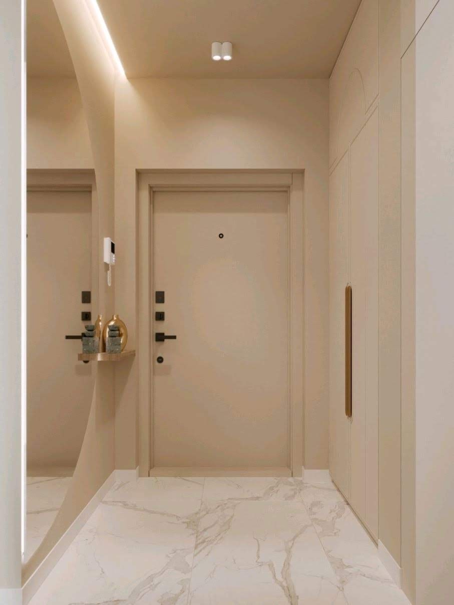 Beżowy przedpokój z marmurową posadzką, minimalistyczną szafą w zabudowie i lustrem z podświetleniem LED, akcentowany złotymi dekoracjami na półce.