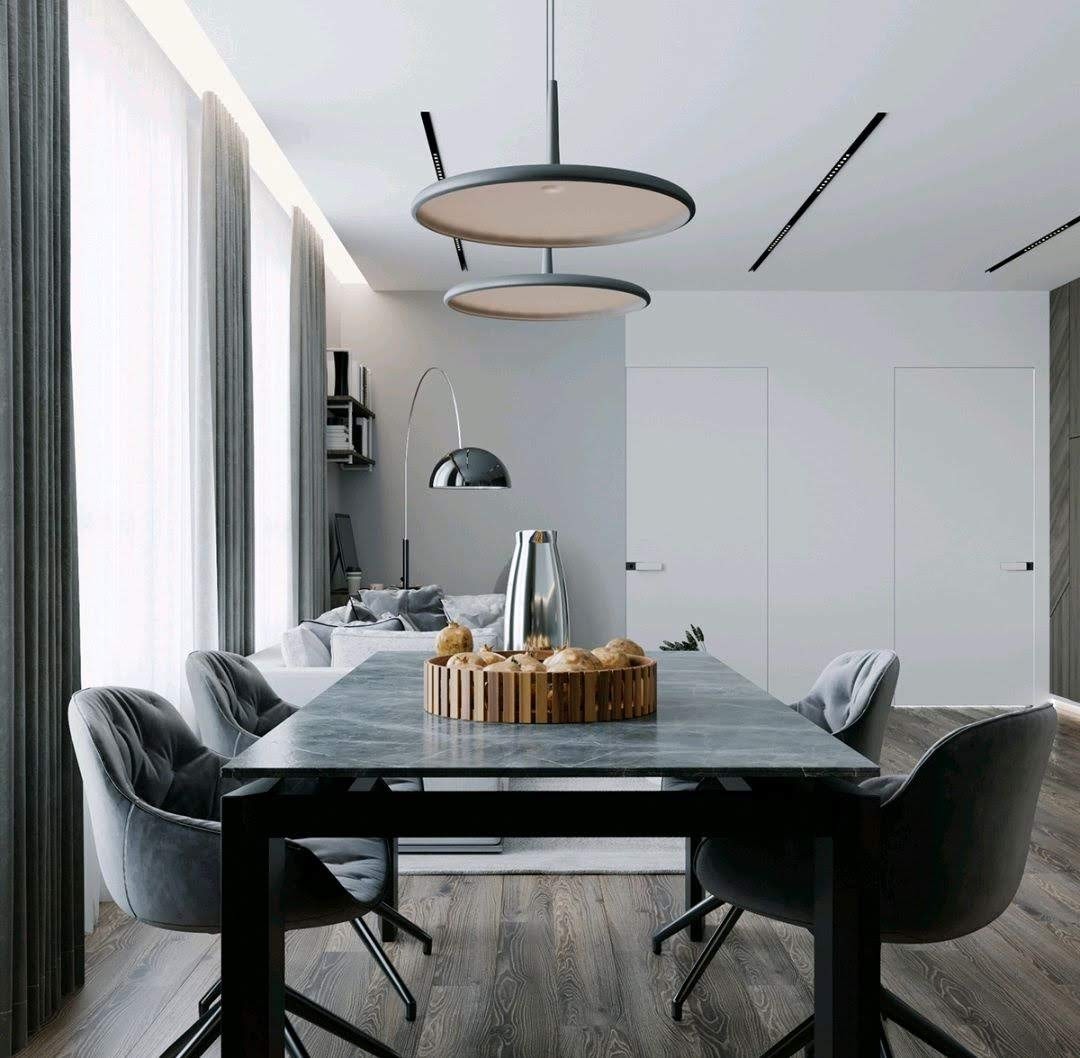 Nowoczesna jadalnia z ciemnoszarym stołem z blatem imitującym kamień, otoczona aksamitnymi krzesłami w kolorze gołębim, z dekoracyjnym oświetleniem sufitowym i widokiem na salon z szarą sofą...
