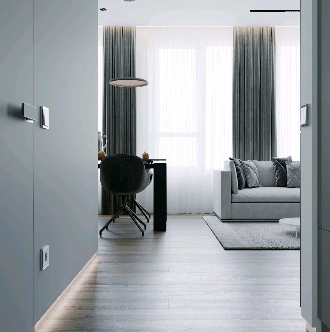 Nowoczesne wnętrze mieszkania w odcieniach szarości: minimalistyczna jadalnia z czarnym stołem i krzesłami, szara sofa z poduszkami, drewniana podłoga i oświetlenie LED wzdłuż ściany.