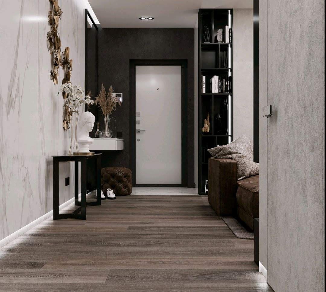 Nowoczesny przedpokój z marmurową ścianą, dekoracyjną rzeźbą głowy na stoliku, ciemną podłogą z paneli, czarnym regałem i brązową sofą.