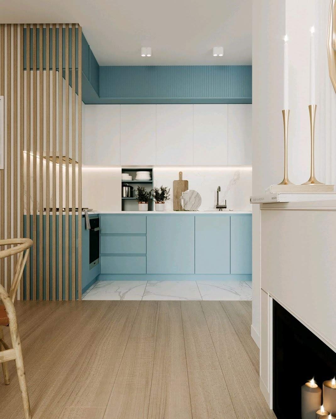 Nowoczesna kuchnia z jasnymi, błękitnymi szafkami, białymi blatami z marmurowym wzorem, drewnianą ażurową ścianką działową i drewnianą podłogą, widziana z perspektywy salonu z kominkiem.
