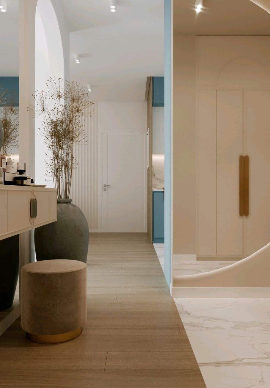 Elegancki przedpokój z drewnianą podłogą, toaletką z szufladami i lustrem, dekoracyjną trawą w dużym wazonie oraz widokiem na pomieszczenie z niebieskimi elementami zabudowy.