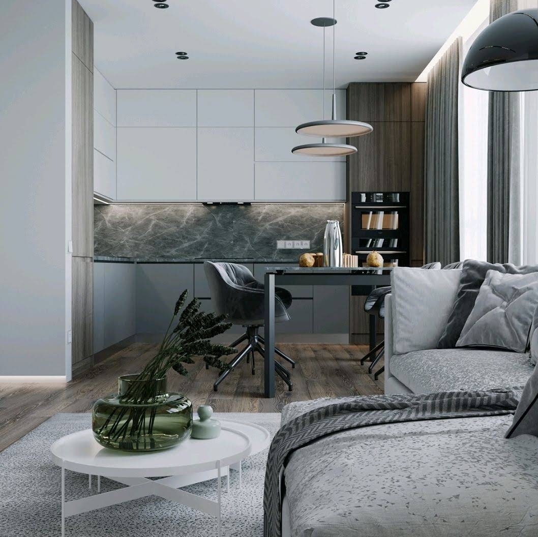 Nowoczesne wnętrze: szaro-biała kuchnia z marmurowym blatem, stół z krzesłami obitymi welurem, sofa z dekoracyjnymi poduszkami i okrągły stolik kawowy z wazonem na dywanie.