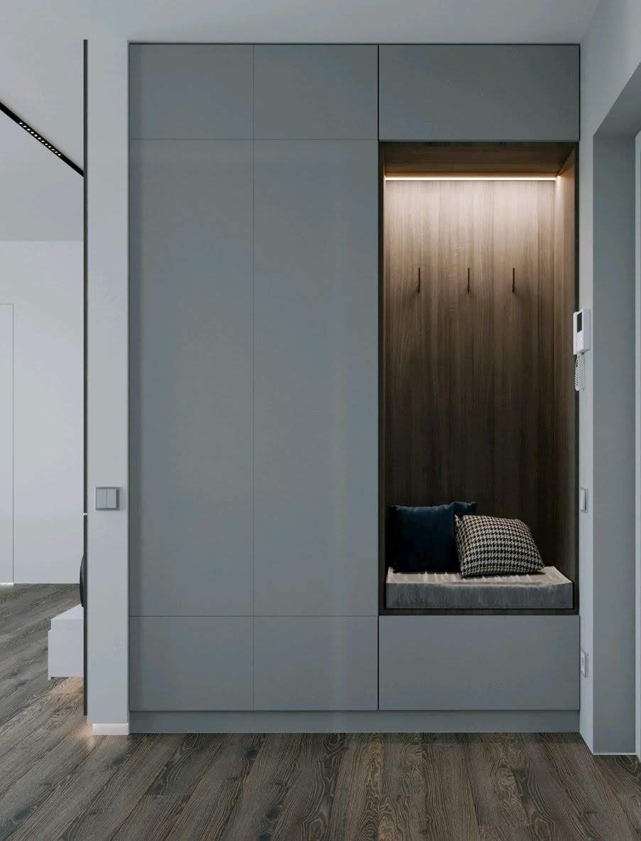 Szara zabudowa w przedpokoju z siedziskiem, drewnianą wnęką z oświetleniem LED i wieszakami, uzupełniona poduszkami w różnych wzorach.