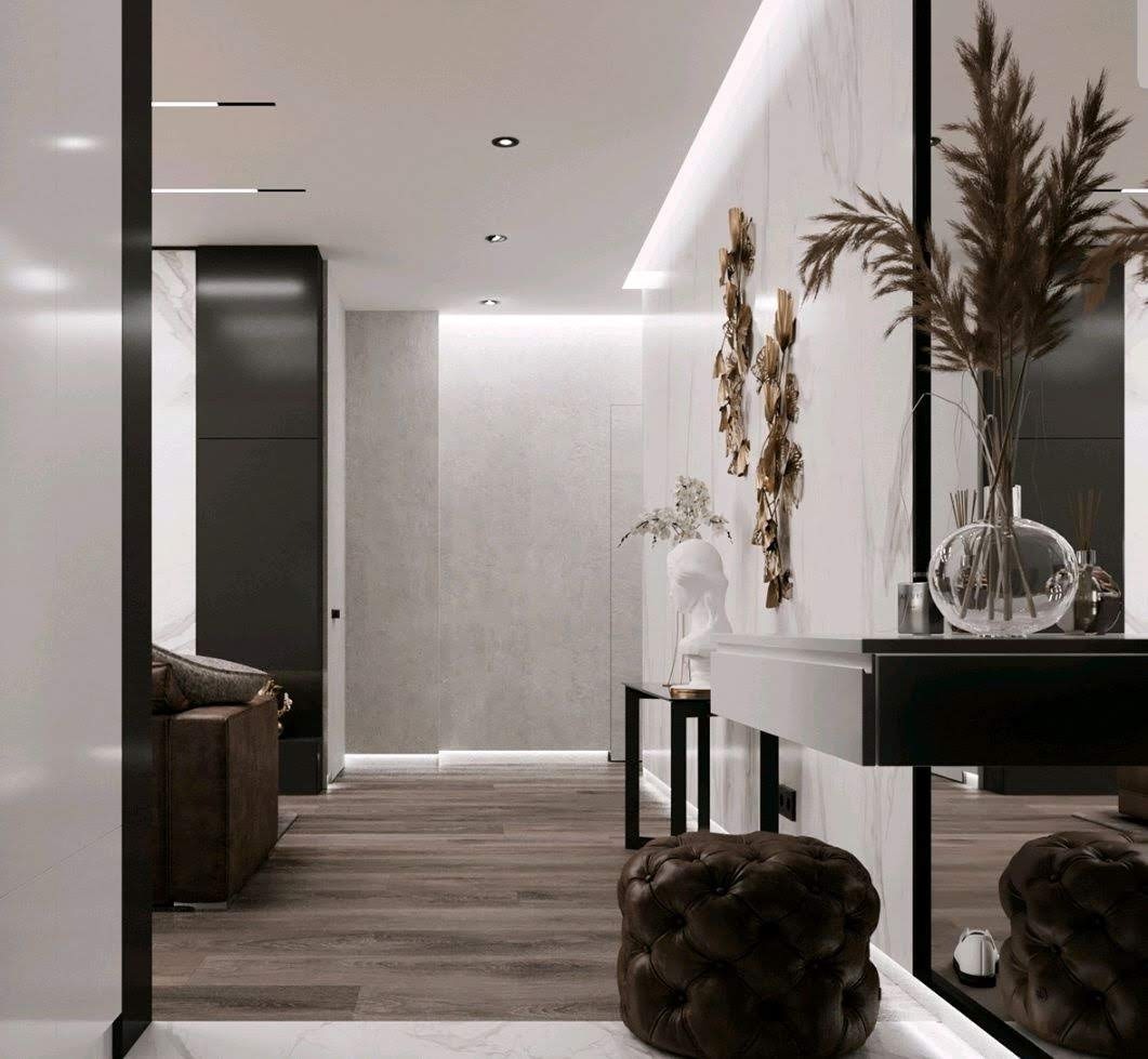 Nowoczesny przedpokój z drewnianą podłogą, marmurową ścianą, dekoracyjną rzeźbą na ścianie, pufem w stylu Chesterfield i lustrem powiększającym przestrzeń.