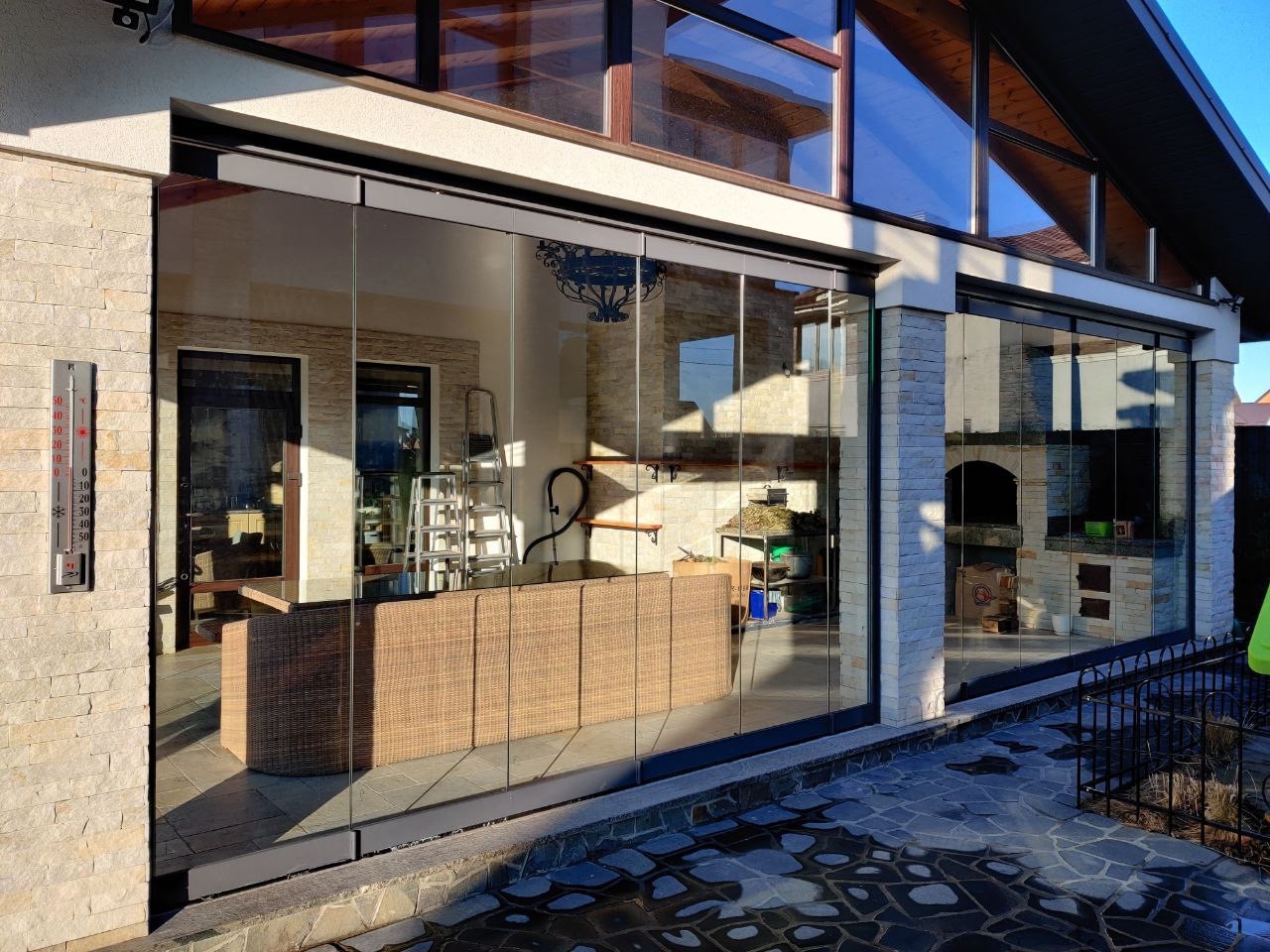 Przeszklona ściana tarasu z przesuwnymi drzwiami, widok z zewnątrz, z widocznym wyposażeniem wnętrza i termometrem na ścianie.