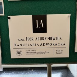 Kancelaria Adwokacka Igor Achrymowicz - Tabliczka informacyjna z danymi kontaktowymi kancelarii adwokackiej Igora Achrymowicza, umieszczona na zielonej tablicy korkowej. Widoczne logo, numer telefonu i adres strony internetowej.