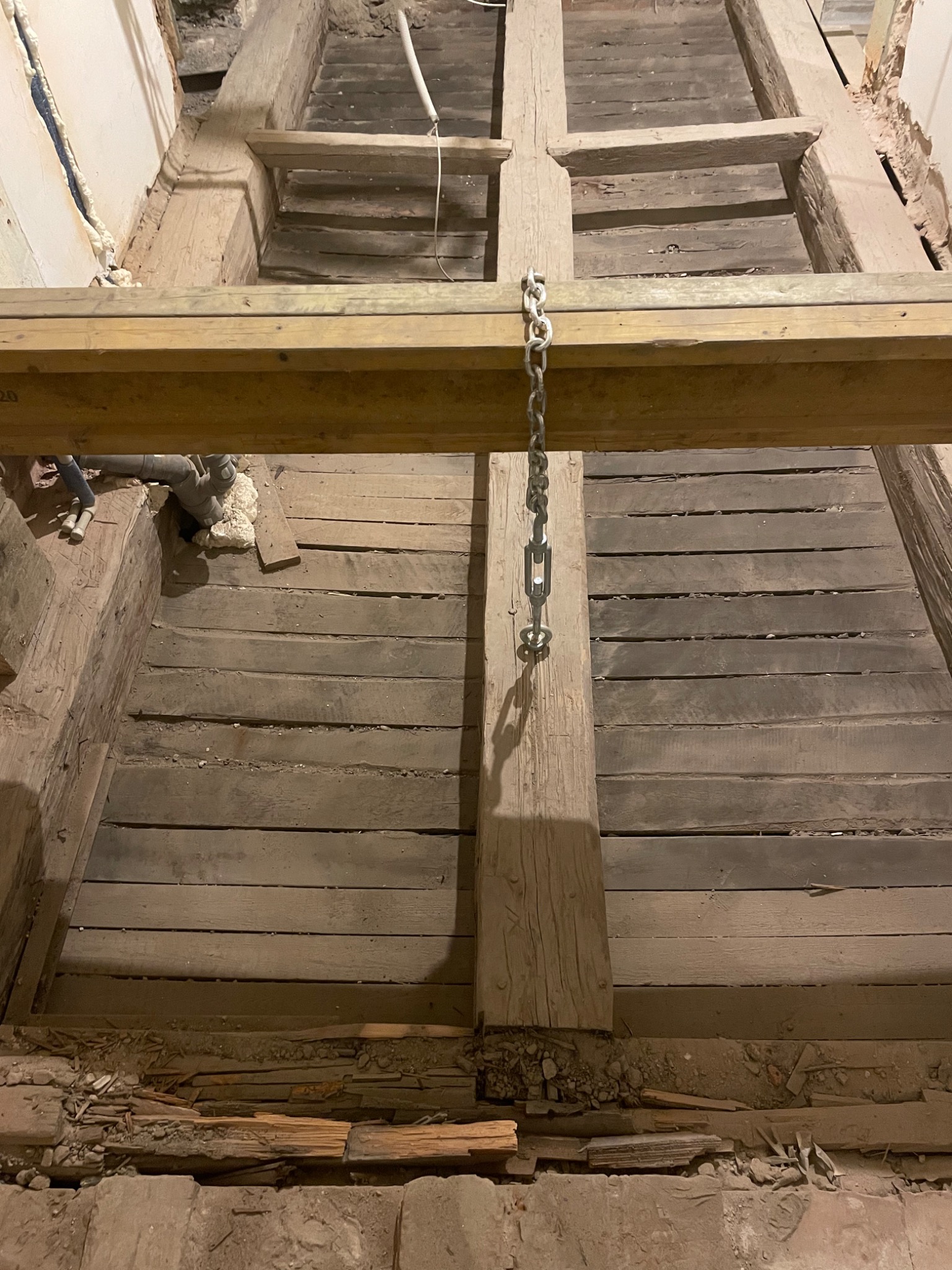 Demontaż drewnianej podłogi z widocznymi belkami stropowymi i łańcuchem podtrzymującym element konstrukcyjny podczas prac rozbiórkowych.