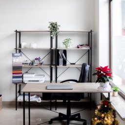 JUST LOOK - Jasne biuro krawieckie z wzornikiem tkanin, biurkiem z laptopem, regałem i dekoracją świąteczną przy oknie. Minimalistyczny wystrój z roślinami.