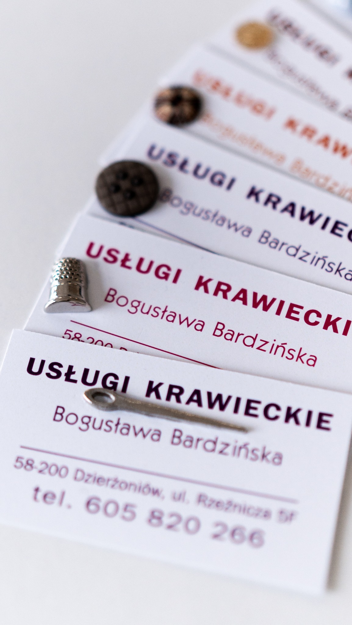 Wizytówki krawieckie z napisem 'Usługi Krawieckie Bogusława Bardzińska', guziki i naparstek. Krawiectwo na miarę w Dzierżoniowie.