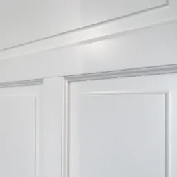 Fragment białych, panelowych drzwi wewnętrznych z delikatnym frezowaniem, oświetlonych równomiernym, naturalnym światłem.