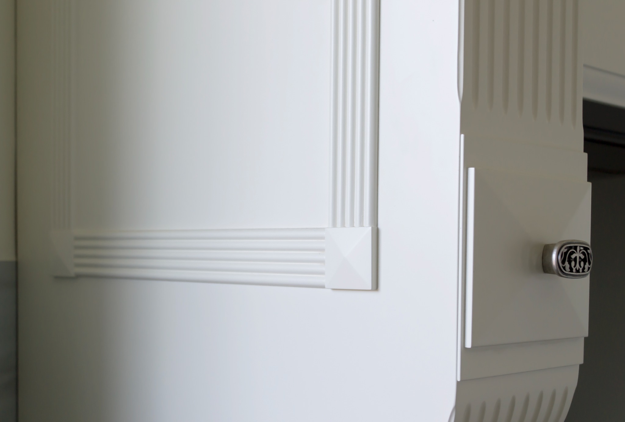 Fragment białej szafki z frezowanymi zdobieniami i ozdobnym uchwytem, wykonanej na wymiar w Sieradzu.