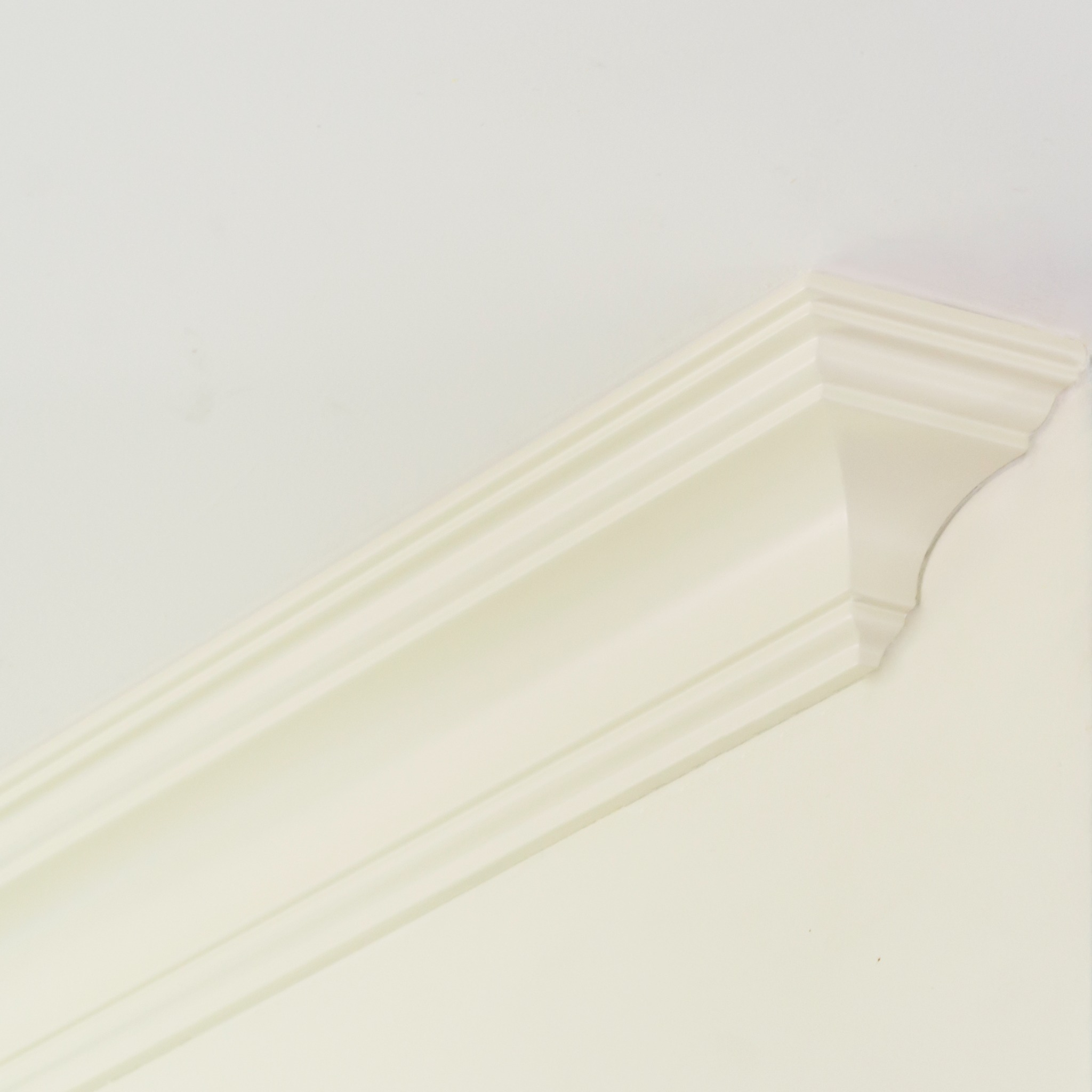 Kremowa listwa przysufitowa z dekoracyjnym profilem zamontowana w rogu pomieszczenia, widok z dołu.