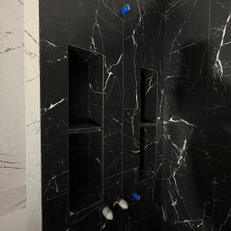 BUD VADYM SYLCHENKO - Czarne płytki imitujące marmur z wnękami w kabinie prysznicowej. Widoczne elementy instalacji wodnej. Minimalistyczny design.