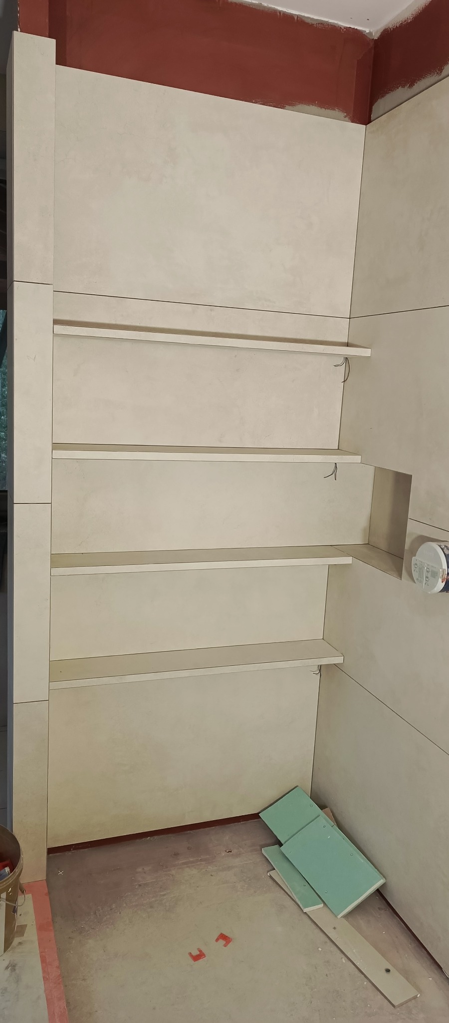 Wnęka z półkami z płyty karton gips, widoczne fragmenty płyt na podłodze, ściany i sufit przygotowane do malowania.