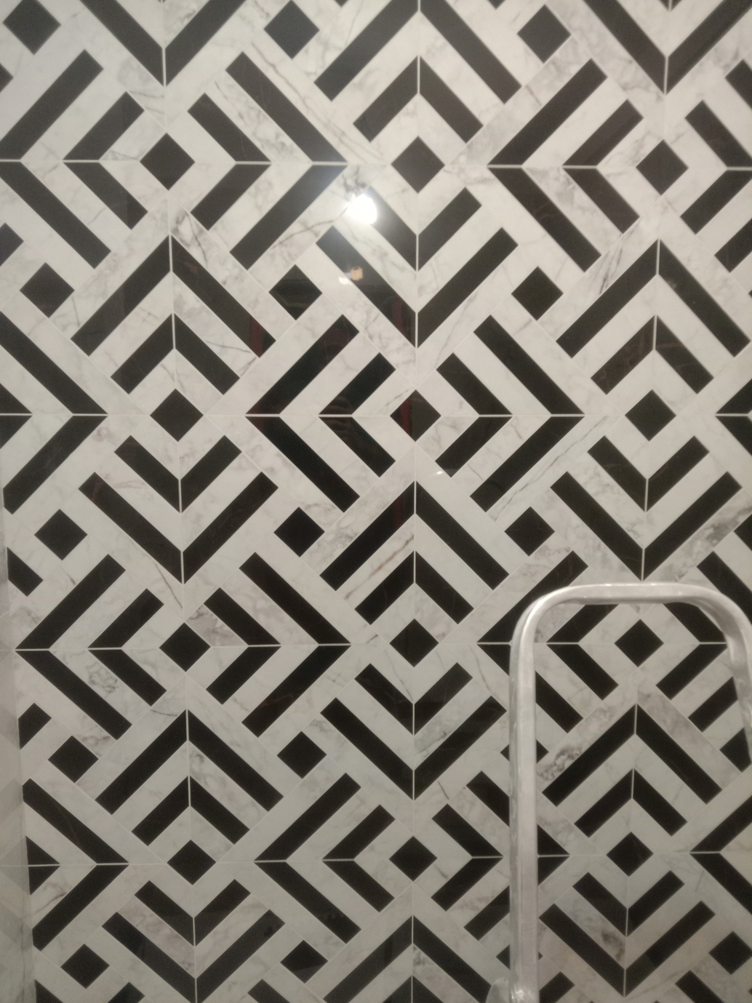 Czarno-biała marmurowa ściana z geometrycznym wzorem w jodełkę, fragment drabiny w prawym dolnym rogu.