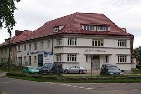 Budynek placówki terapeutycznej z czerwonym dachem, widoczne zaparkowane samochody i tablice informacyjne przed wejściem.