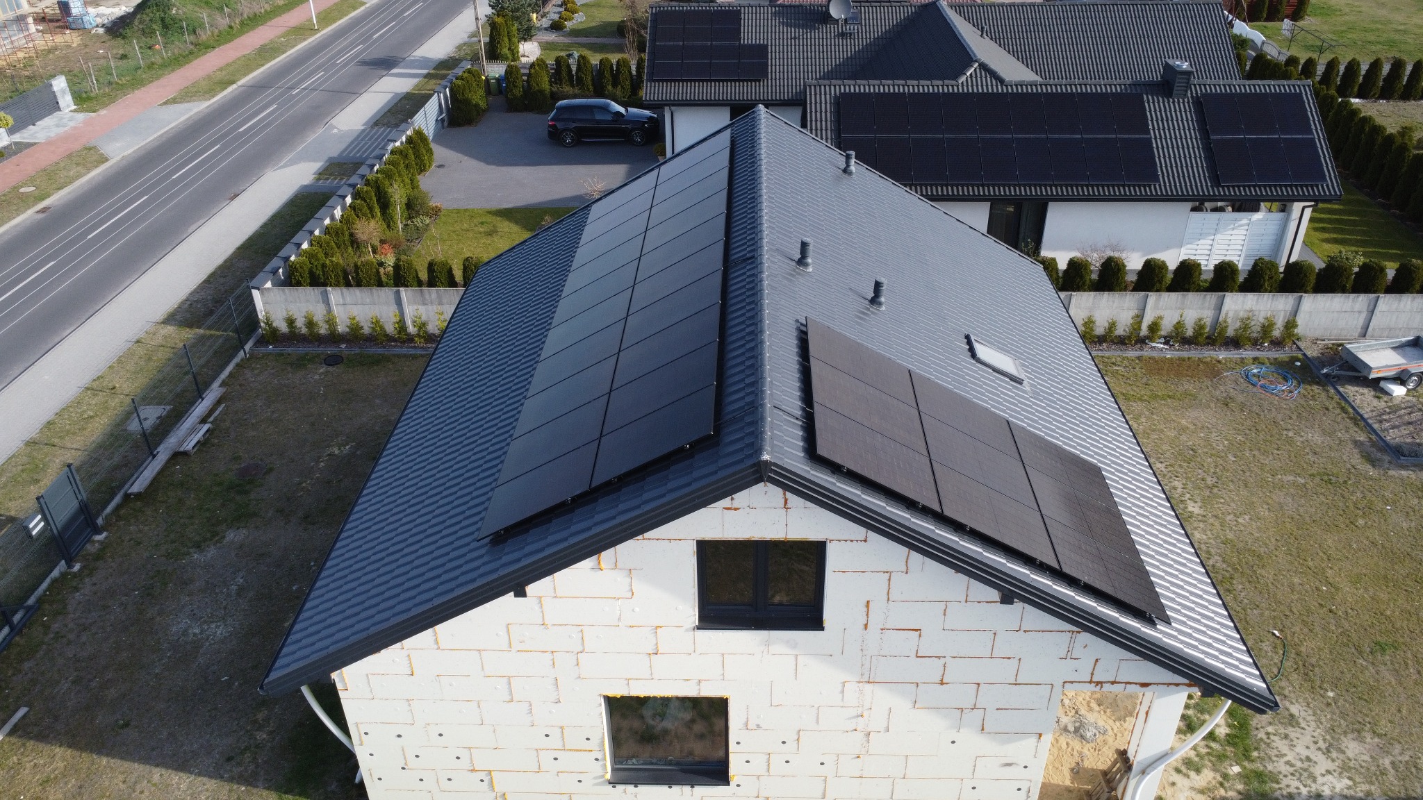 Widok z góry na dom w trakcie budowy z zamontowanymi panelami fotowoltaicznymi na dachu z blachy trapezowej w kolorze grafitowym. Widoczne okna i ocieplenie budynku.