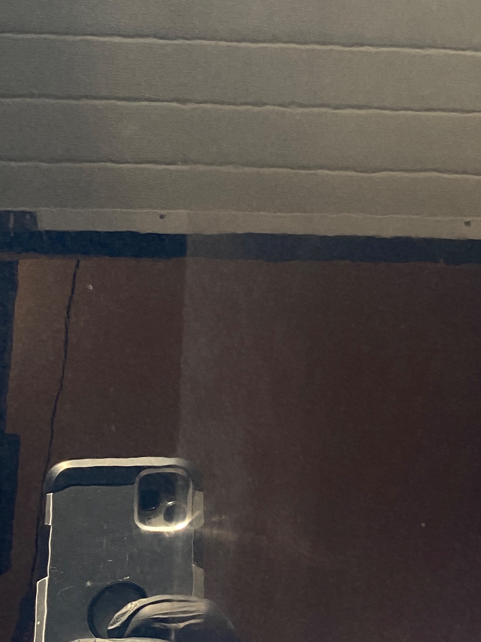 Odbicie telefonu w brudnej, pionowej powierzchni z poziomymi wgłębieniami u góry.