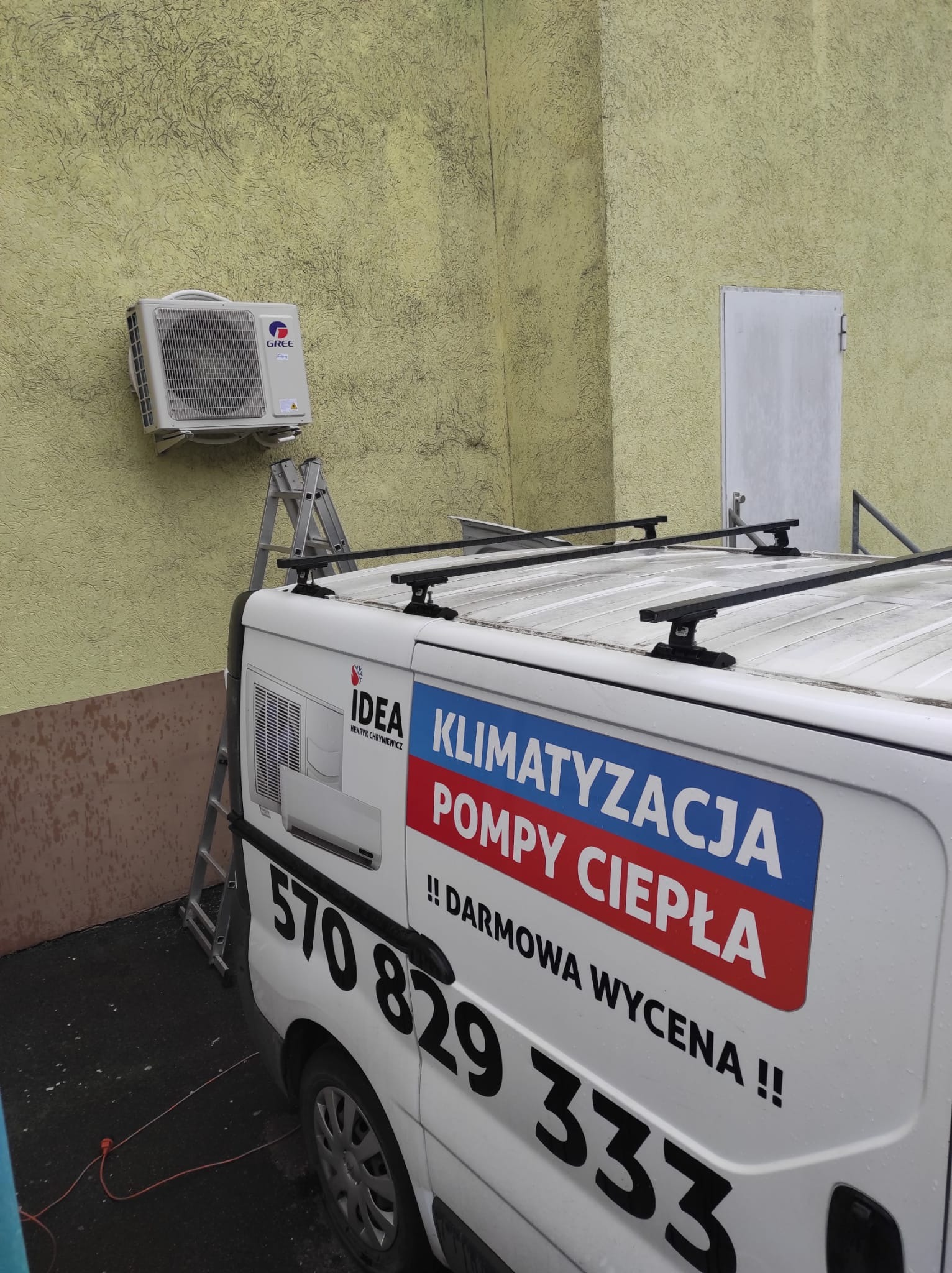Zamontowany klimatyzator GREE na elewacji budynku, obok drabina i samochód dostawczy z reklamą firmy oferującej montaż klimatyzacji i pomp ciepła.