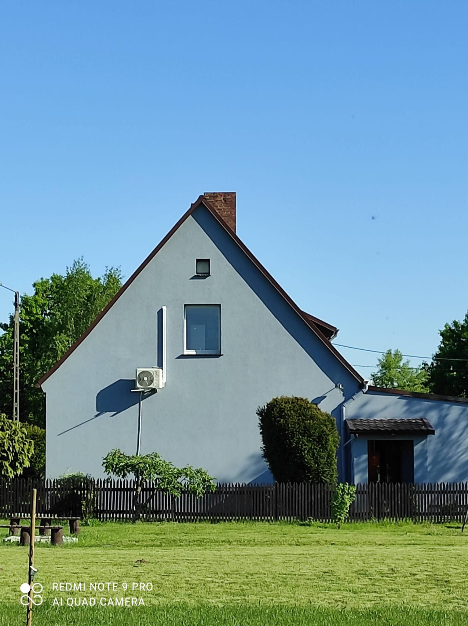 Niebieski dom jednorodzinny z zamontowaną klimatyzacją na ścianie, widok z zewnątrz, błękitne niebo w tle.