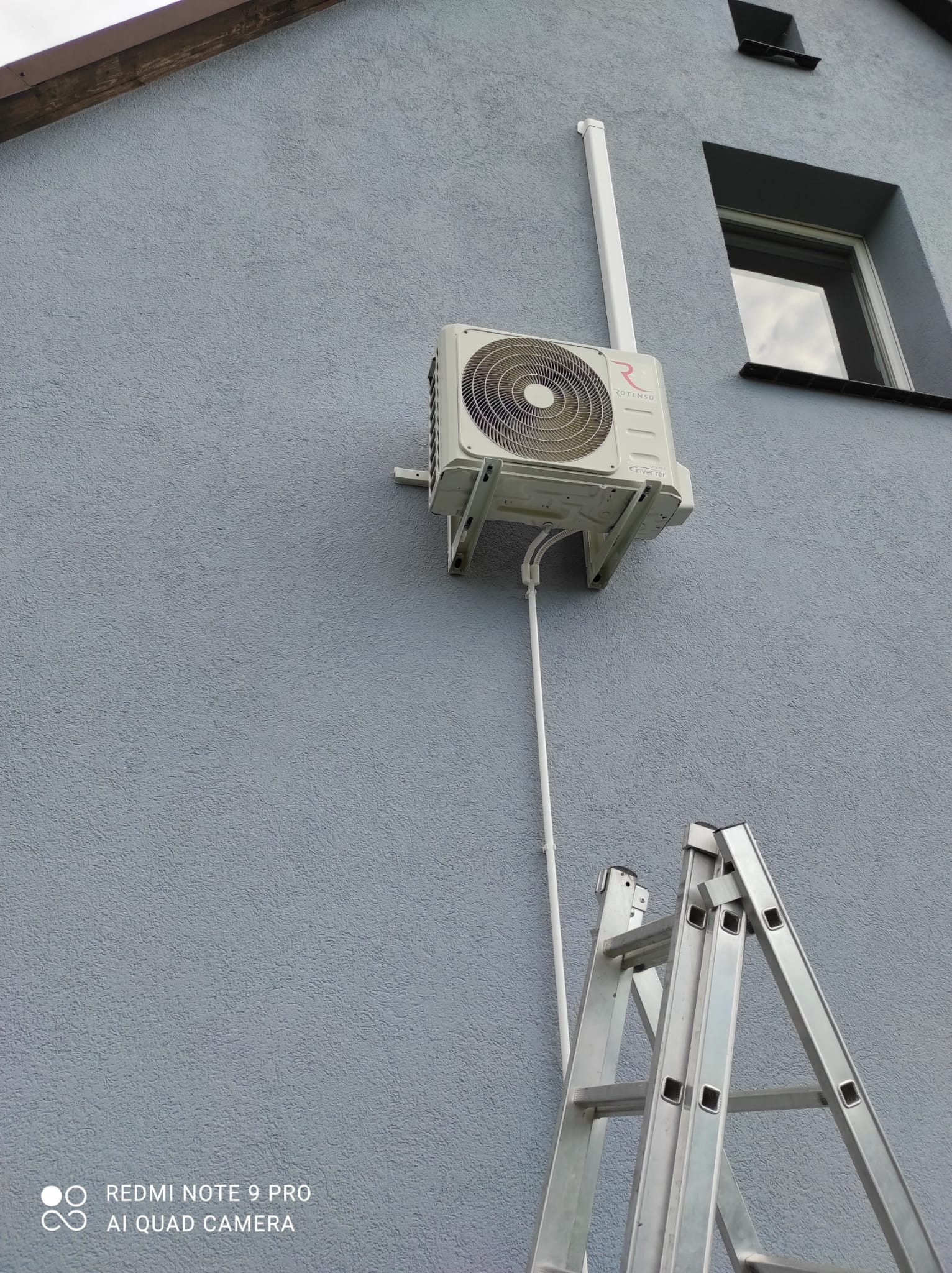 Zamontowana jednostka zewnętrzna klimatyzacji Rotenso na szarej elewacji budynku, widoczna drabina aluminiowa.