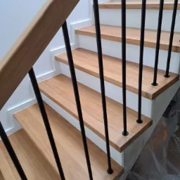 Schody drewniane z jasnego drewna z czarnymi, metalowymi balustradami, widok z góry, zabezpieczone folią malarską.