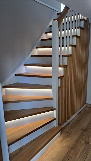 Nowoczesne schody z drewna z białymi podstopnicami i podświetleniem LED, drewniana balustrada z pionowych listew.