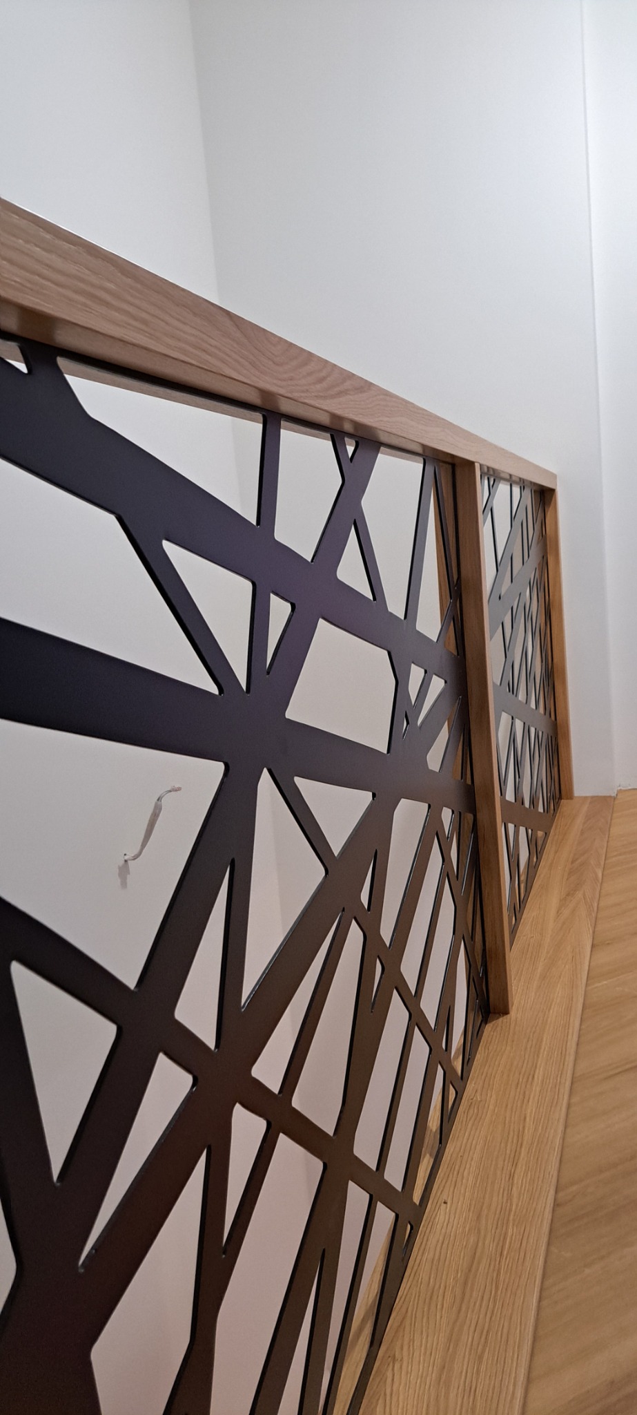 Nowoczesna balustrada schodowa z czarnym, geometrycznym wzorem i drewnianym wykończeniem, widok z dołu ukazujący detale konstrukcji.